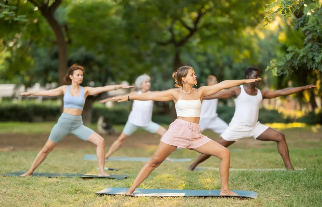 group enjoying yoga in morning group class on green shaded lawn in summer park
